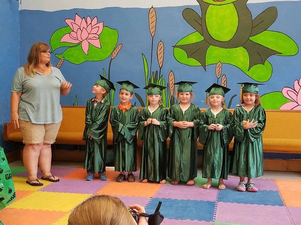 Children in green graduation gowns celebrating a preschool program at a quality childcare center